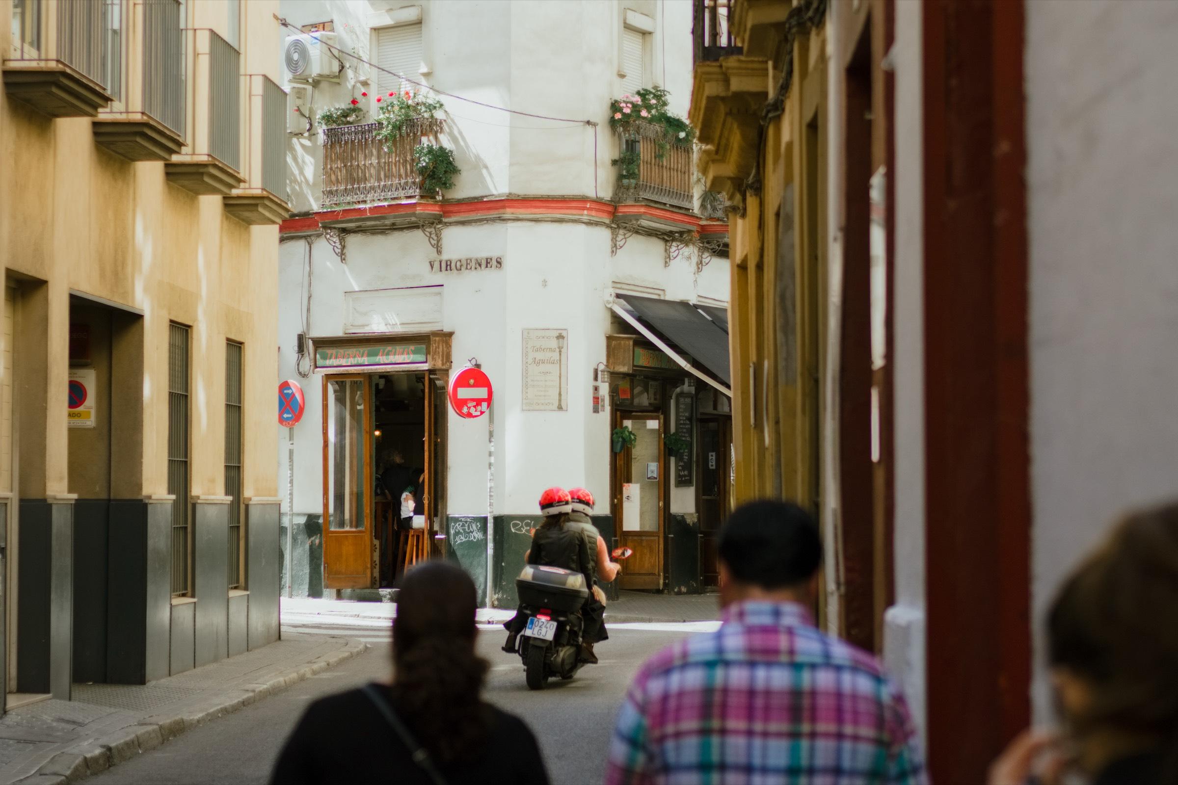 A street corner in central Seville, with a taberna, flower-filled balconies and a scooter going by.